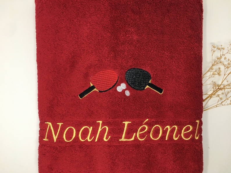 May include: Red towel with embroidered ping pong paddles and the name "Noah L&eacute;onel" in gold thread.