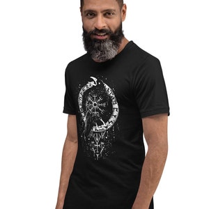 May include: A black t-shirt featuring a white graphic design of a raven, a compass, and runes. The design is centrally positioned on the shirt.