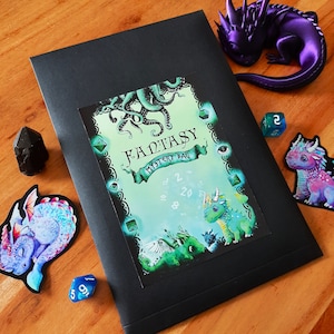 Könnte beinhalten: Ein schwarzer Umschlag mit einer grünen und blauen Fantasy-Karte darin. Die Karte zeigt einen grünen und blauen Drachen auf weißem Hintergrund mit dem Text "Fantasy Mystery Bag".