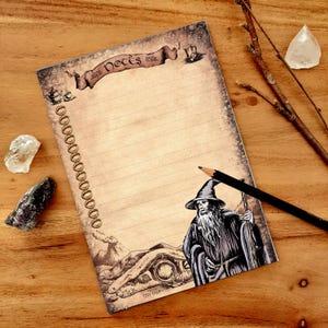Può includere: Un blocco note dal design vintage con un'illustrazione di un mago e la parola "Notes" su uno striscione. Il blocco note ha pagine a righe e una matita. Lo sfondo è una superficie di legno.