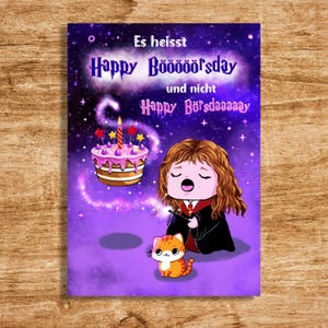 Op de afbeelding: Een paarse verjaardagskaart met de tekst "Es heisst Happy Böööööörsday und nicht Happy Bürsdaaaaaay". De kaart toont een cartoon illustratie van een personage met een toverstaf, een taart en een kat.