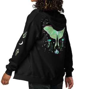 May include: Black zip-up hoodie featuring a large green moth design on the back. The moth is surrounded by mushrooms, crystals, and stars. The left sleeve has a crescent moon and sprigs. A hooded sweatshirt.
