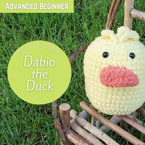 Può includere: Un giocattolo di peluche di anatra gialla all'uncinetto con un becco rosa e occhi neri. L'anatra è seduta su una sedia di legno. Il testo "PDF Crochet Pattern Dabio the Duck" è su un cerchio verde.