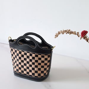 May include: A black and tan checkered leather handbag with a top handle and a shoulder strap.