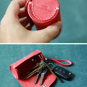 May include: Red leather key holder with a white stitched seam and the text "Pursuit Delicacy Handmade" on the top. The key holder is open and filled with keys.
