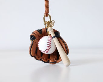 May include: A brown leather baseball glove keychain with a white baseball and a wooden bat.