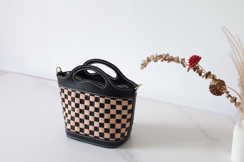 May include: A black and tan checkered leather handbag with a top handle and a shoulder strap.