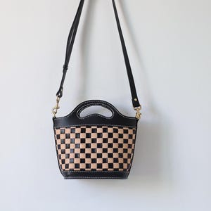 May include: A black leather handbag with a checkered pattern in black and tan. The bag has a top handle and a long shoulder strap.