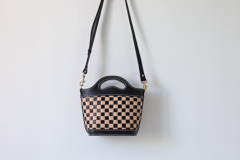 May include: A black leather handbag with a checkered pattern in black and tan. The bag has a top handle and a long shoulder strap.