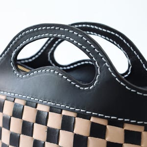 May include: A black leather handbag with a checkered pattern in black and tan. The bag has a unique design with two cut-out handles.
