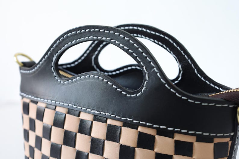 May include: A black leather handbag with a checkered pattern in black and tan. The bag has a unique design with two cut-out handles.