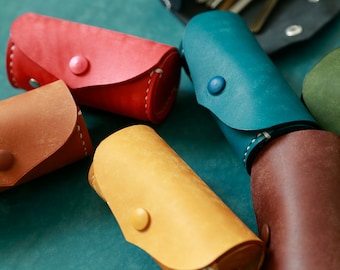 Könnte beinhalten: Sechs Leder-Schlüsselanhänger in verschiedenen Farben, darunter Rot, Braun, Gelb, Grün, Blau und Braun. Jeder Schlüsselanhänger hat einen Knopfverschluss.