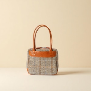 Może przedstawiać: Mała, kwadratowa torebka z wzorem w kratę w kolorze szarym, brązowym i białym. Torba posiada brązowe skórzane akcenty na górze i na dole, z pasującymi uchwytami. Torba stoi na białej powierzchni.