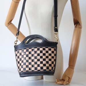 May include: A black and tan checkered leather handbag with a black leather strap. The bag has a top handle and a shoulder strap.