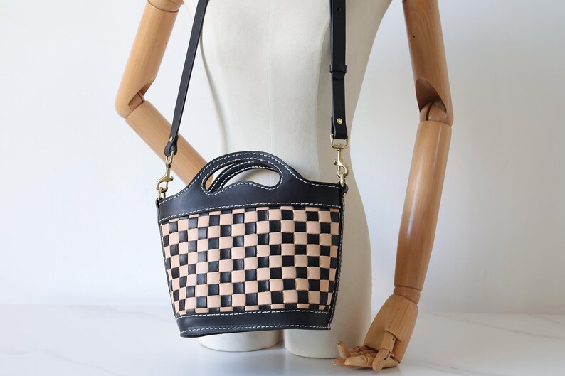 May include: A black and tan checkered leather handbag with a black leather strap. The bag has a top handle and a shoulder strap.
