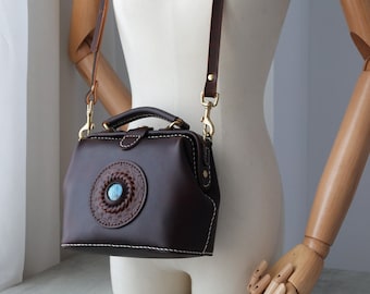 May include: A brown leather doctor bag with a decorative circular design featuring a blue stone in the center. The bag has a long strap and a top handle.