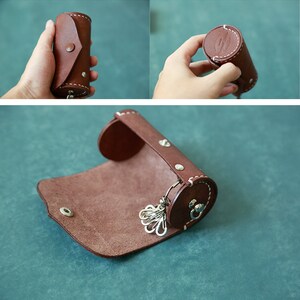 May include: A brown leather key holder with a rolled design and a metal key ring. The key holder is open and the key ring is visible.