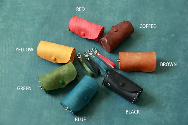 May include: Assortment of ten leather keychains in various colours, including red, yellow, green, blue, black, brown, and coffee. Each keychain features a small leather pouch with a button closure and a metal ring.