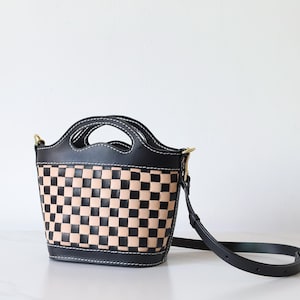 May include: A black and tan checkered leather handbag with a top handle and a long shoulder strap.