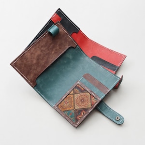 May include: A multi-colored leather wallet featuring a teal interior, a brown textured pocket, and a square card slot with a geometric pattern. The wallet includes a red section, white contrast stitching, and a snap button closure on a teal strap.