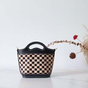 May include: A black and tan checkered leather handbag with a top handle and a short shoulder strap.