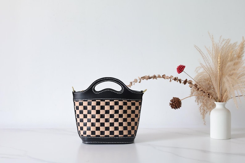 May include: A black and tan checkered leather handbag with a top handle and a short shoulder strap.