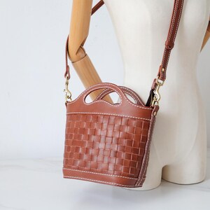 Puede incluir: Bolso bandolera de cuero marr&oacute;n con dise&ntilde;o tejido. El bolso tiene un asa superior y una correa para el hombro desmontable. El bolso mide aproximadamente 20 cm de alto y 18 cm de ancho. El bolso se muestra en un maniqu&iacute;.
