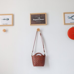 Puede incluir: Una exhibici&oacute;n montada en la pared con impresiones enmarcadas de herramientas y un reloj. Una bolsa de mano marr&oacute;n tejida cuelga debajo de las impresiones. El reloj es redondo, rojo y tiene manecillas doradas. Las impresiones est&aacute;n en marcos de madera.