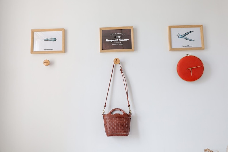 Puede incluir: Una exhibici&oacute;n montada en la pared con impresiones enmarcadas de herramientas y un reloj. Una bolsa de mano marr&oacute;n tejida cuelga debajo de las impresiones. El reloj es redondo, rojo y tiene manecillas doradas. Las impresiones est&aacute;n en marcos de madera.