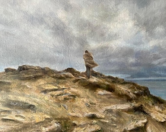 May include: An oil painting depicts a person standing on a rocky hill, facing away from the viewer. The person is wearing a tan coat, with the wind blowing it. The sky is overcast, and the sea is visible in the distance.