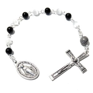 May include: A silver rosary with black, white, and gray beads. The rosary features a silver crucifix and a silver medal with the image of the Virgin Mary and the text "O Mary Conceived Without Sin Pray for Us Who Have Recourse to Thee".