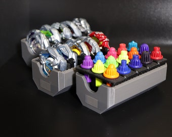 May include: A gray plastic storage case with compartments for holding small toys. The case has two sections, one for holding spinning tops and the other for holding small colorful plastic pieces.