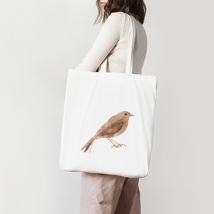 K&ouml;nnte beinhalten: Eine wei&szlig;e Einkaufstasche mit einer braunen Aquarell-Vogel-Illustration. Die Tasche hat zwei lange Henkel.