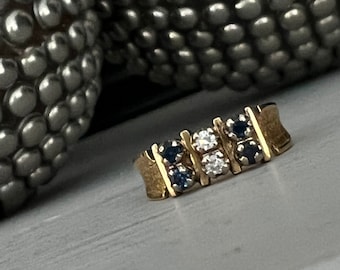 May include: A gold band ring with a row of small blue gemstones and a single larger clear gemstone in the centre.