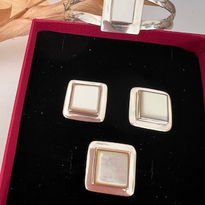 Könnte beinhalten: Ein Set aus drei Silberringen mit weißen Perlmutteinlagen. Die Ringe werden in einer roten Samtbox präsentiert.