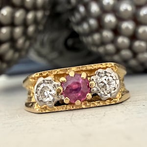 Peut inclure: Une bague en or avec une pierre rose centrale flanquée de deux pierres blanches. La bague a une bande en or texturée et une esthétique vintage. Les pierres sont serties dans un métal blanc contrastant.