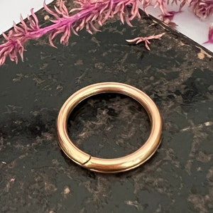 Puede incluir: Un aro para pendientes de color dorado con un acabado impecable. El aro está sobre una superficie oscura y texturizada.
