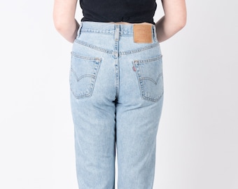 May include: A pair of light blue denim jeans with a high waist and a straight leg fit. The jeans have a classic five-pocket design and a leather patch on the back waistband with the Levi's logo.