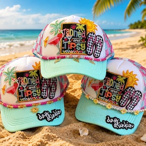 May include: Three trucker hats with light blue brims and white front panels featuring a colorful patch that reads Tanned and Tipsy. The design includes palm trees, a cocktail, and flip-flops. Each hat has beaded trim and a black patch reading day drinkin.