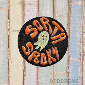 May include: A round black patch with the words "SORTA SPOOKY" in orange, outlined in purple, and a light green ghost in the center. The patch is a Halloween-themed design.