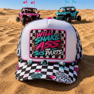 May include: A white and black checkered trucker hat featuring a rectangular patch with the text WILL SHAKE ASS FOR SXS PARTS in pink and teal. The hat includes a beaded cord with an eight-ball and dice accents across the brim base.