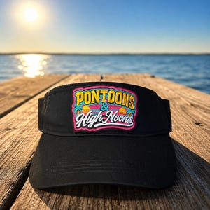 May include: A black visor featuring an embroidered patch on the front. The patch displays the text PONTOONS & HIGH NOONS in yellow and white lettering, accented by pink, teal, and orange graphics of palm trees and a sunset over water.