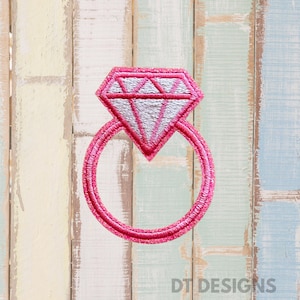 May include: A pink embroidered patch in the shape of a diamond ring. The ring features a large, pink diamond with a silver interior and a pink band. The patch is set against a backdrop of pastel-colored wooden planks.