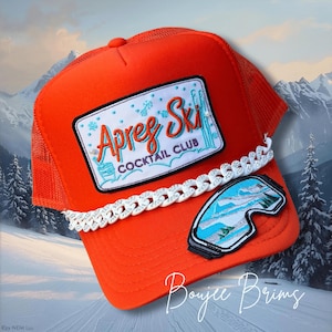 May include: Bright orange trucker hat with a white chain and patches. The main patch reads "Apres Ski Cocktail Club" with ski graphics. A second patch shows ski goggles. The hat has a mesh back and a curved brim.