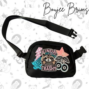 May include: Black fanny pack with a decorative patch featuring a raccoon, lightning bolt, star, and cherries. The patch includes the phrases "Kinda Classy" and "Kinda Trashy". The bag has an adjustable black strap.