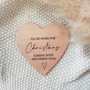 May include: A wooden heart-shaped sign with the text "I'll be home for Christmas coming soon -December 2025-." The sign is on a white knitted surface.