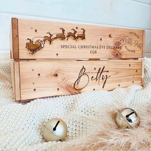 Puede incluir: Una caja de madera con un tema de entrega de Nochebuena. La caja está decorada con un diseño de renos y Papá Noel y el texto "Special Christmas Eve Delivery for Betty". La caja está sentada sobre una manta blanca y peluda.