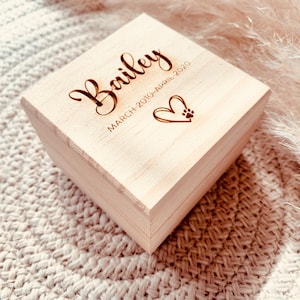 May include: A light wood box with the name "Bailey" engraved on the top, along with the dates "March 2010 - April 2020". A heart with a paw print is also engraved on the box.