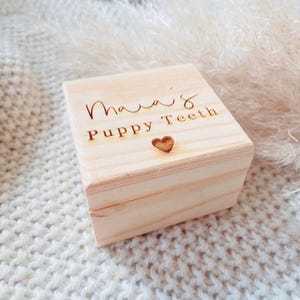 May include: A small wooden box with the inscription "Maia's Puppy Teeth" and a heart cutout. The box is light brown and has a natural wood finish.