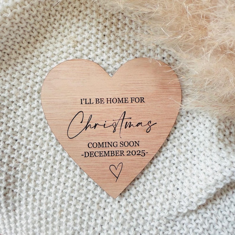 May include: A wooden heart-shaped sign with the text "I'll be home for Christmas coming soon -December 2025-." The sign is on a white knitted surface.